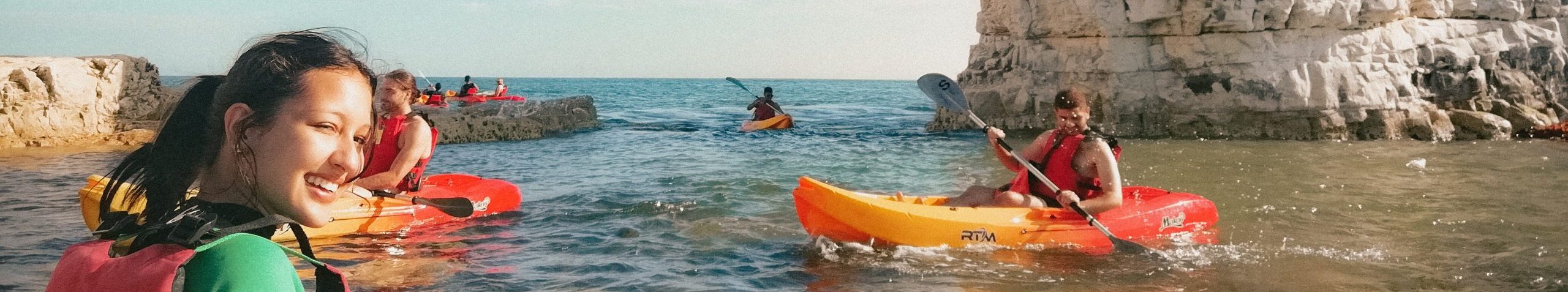 A girl is looking at the camera. She is in a small boat in the ocean. To her right, another male student is rowing.