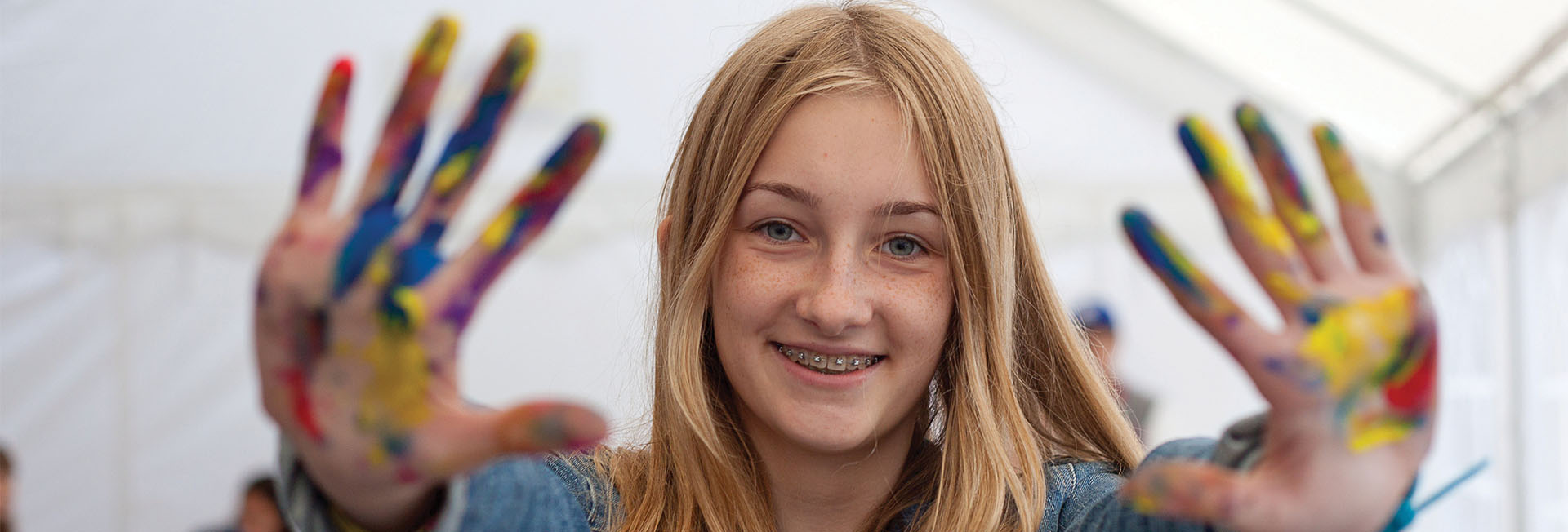 A junior student holds her hands up to the camera, showing finger paint